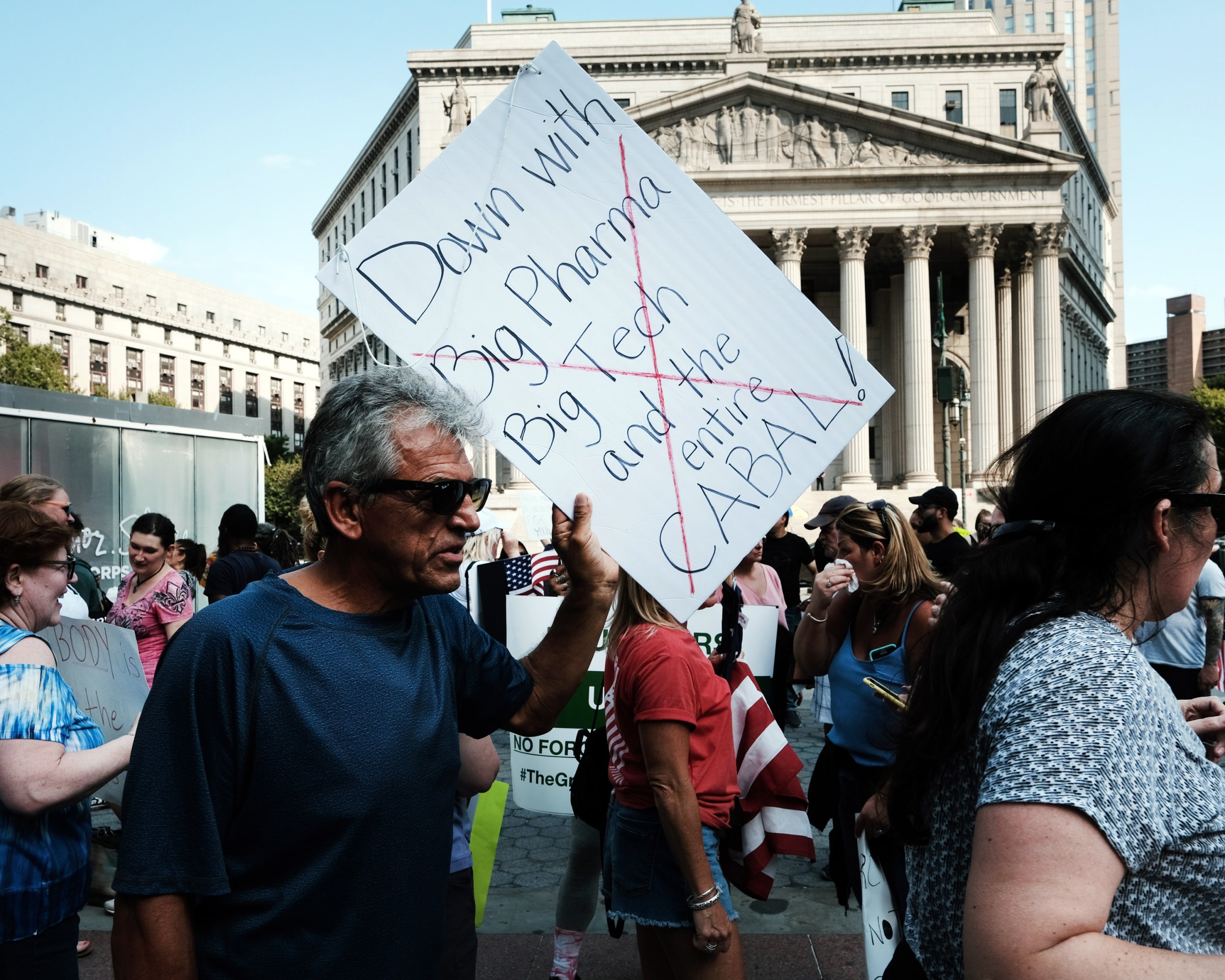 People participate in a rally and march against COVID-19 mandates in NYC. Man in foreground holds sign that reads, "Down with Big Pharma, Big Tech and the entire Cabal."