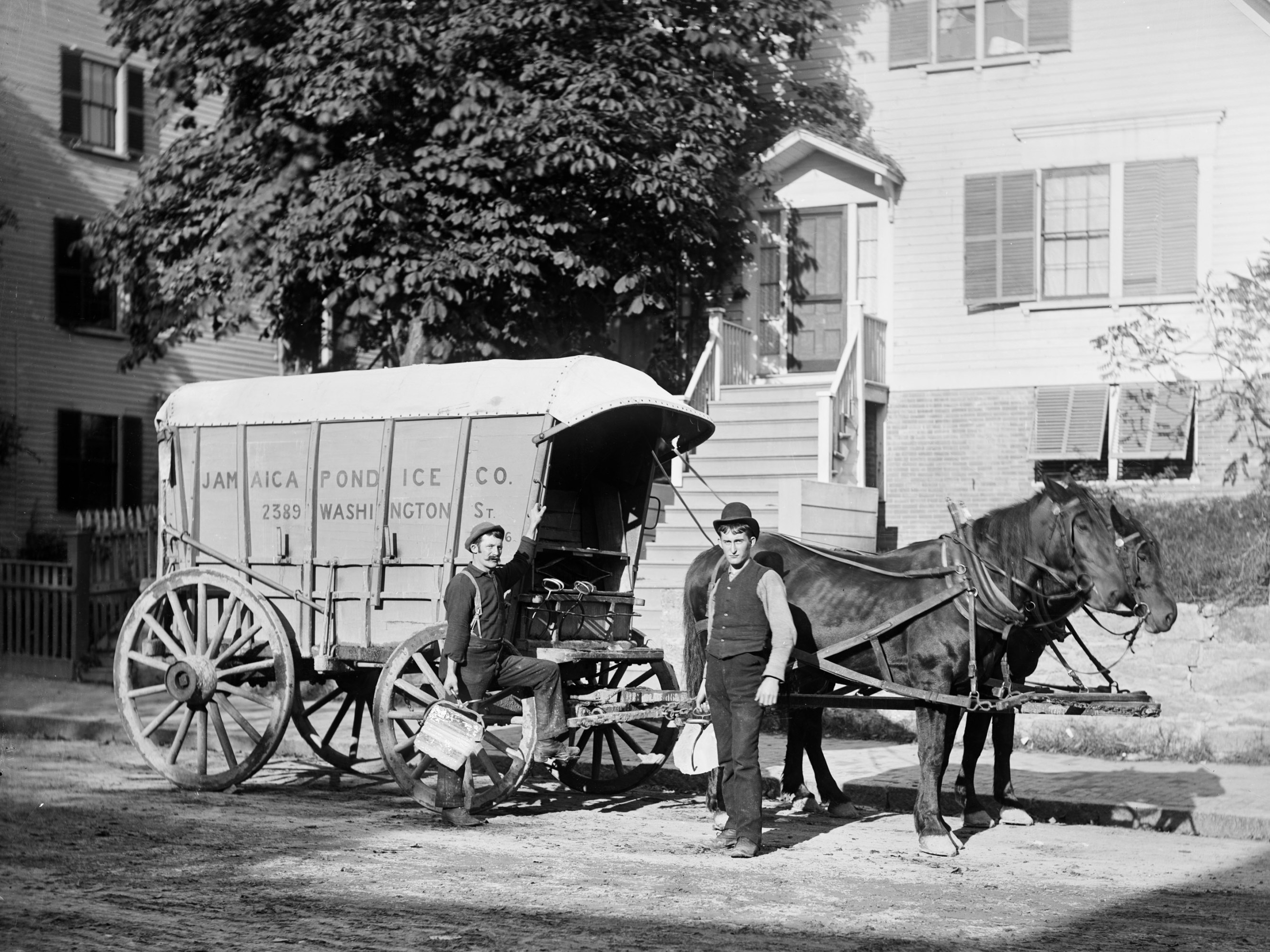 Two men standing next to a horse-drawn carriage with "Jamaica Plain Ice Co" painted on the side